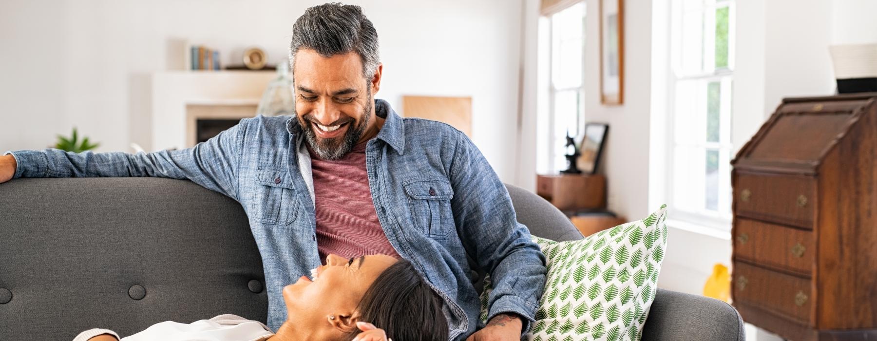 a couple laughing on a couch in a bright room